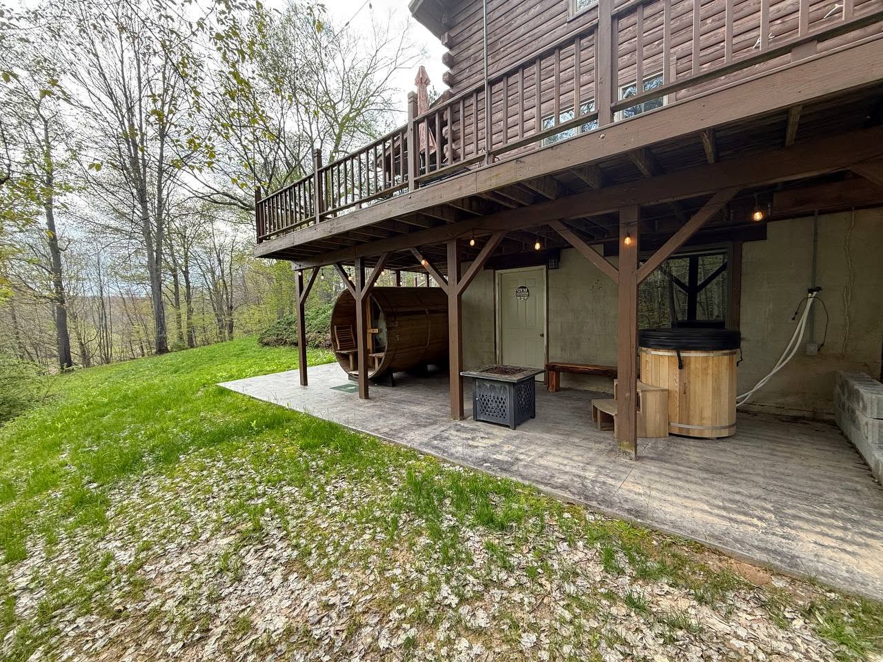 Daylight side view of the barrel sauna and cold plunge beneath the cabin deck